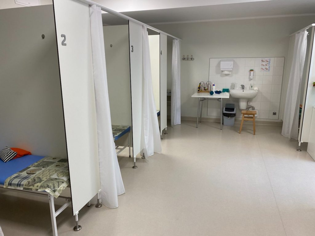 Zdjęcie przedstawiające pomieszczenie do wykonywania zabiegów rehabilitacyjnych. W pomieszczeniu znajduje się 8 kabin w których znajdują się różne urządzenia do zabiegów. Każda kabina ma możliwość zasłonięcia kotarą.